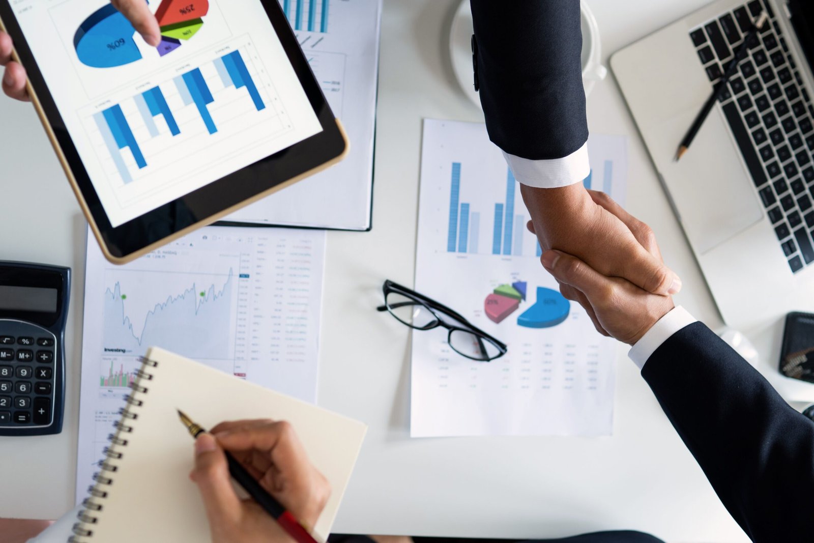 our-services-02 Business professionals handshake over graphs and charts in a corporate setting, symbolizing successful negotiation and agreement.