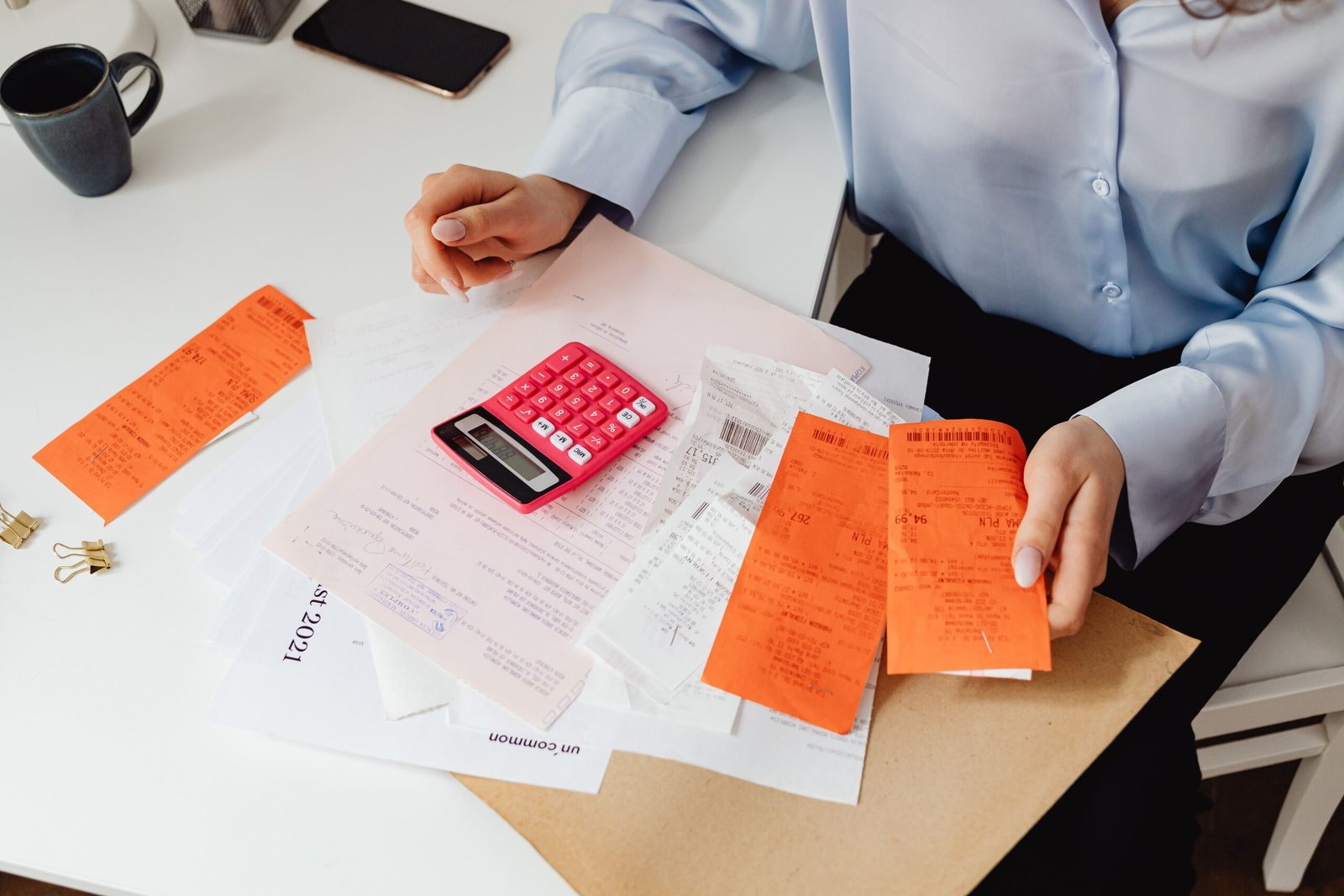 our-services-01 A woman reviews receipts and calculates expenses at a desk with a pink calculator.